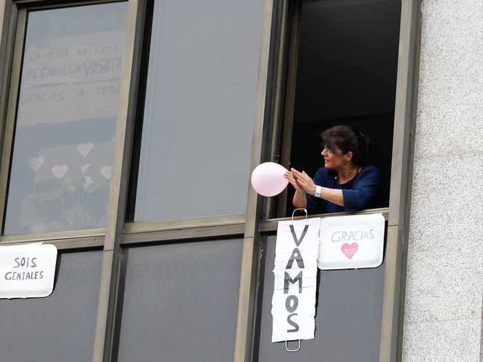 Even hospital patients have taken to their windows to applaud. At a makeshift hospital site in Madrid, a woman is seen holding a balloon above encouraging signs for healthcare workers.