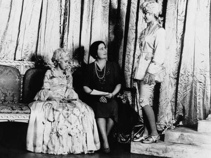 1941: Princess Elizabeth discusses the pantomime with her mother, Queen Elizabeth of England, while her sister, Princess Margaret, looks on. The two princesses took the leading roles in the show and also produced the play for the benefit of the Royal Household Concert Wool Fund.