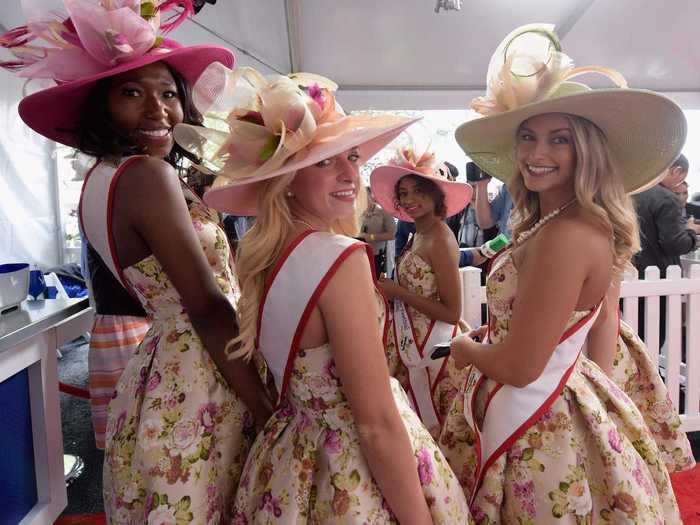 Kentucky Derby Princesses and Queens posed in matching floral dresses and pink wide-brimmed hats.