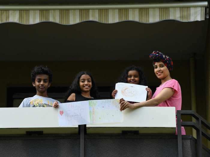 In Munich, Germany, three siblings pose outside with their mother, holding up drawings that show they miss going to school and playing outside in nature.