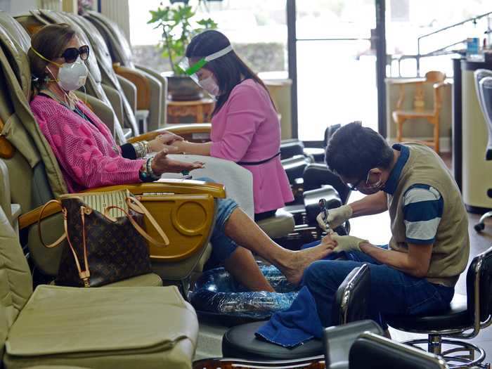 Jeannie Dent talks to a customer across the room as she gets a manicure from Sally Le and pedicure from Tom Dinh at Nail Turbo, during the phased reopening of businesses and restaurants from coronavirus disease (COVID-19) restrictions in the state, in Roswell, Georgia.