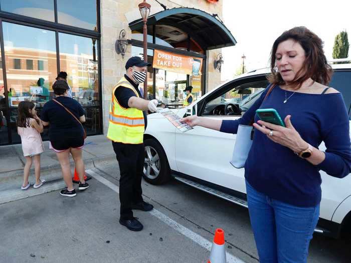 A woman waiting in a social distancing line marked by orange traffic cones at Costa Vida takes a menu from an employee.