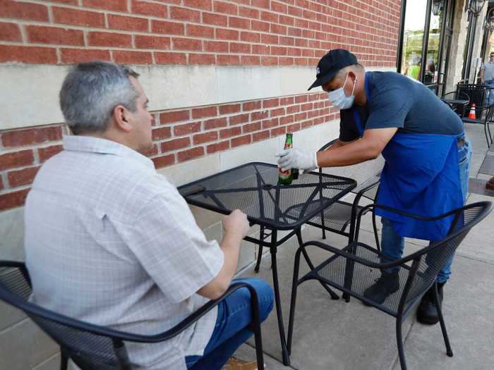 A masked server delivers a beer to a diner on the patio of Costa Vida.