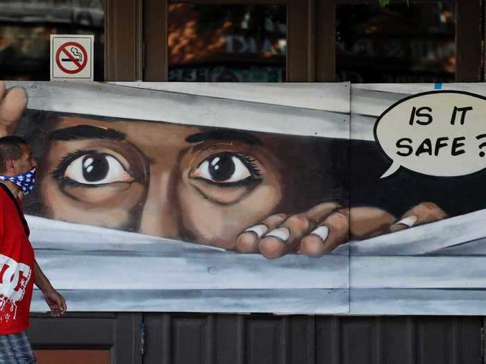 A man wearing a bandana as a protective covering walks past a series of coronavirus-related murals in Austin, Texas.