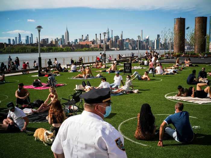 A New York Police Department officer keeps an eye on people as they control social distance on a warm day during the outbreak of the coronavirus disease.