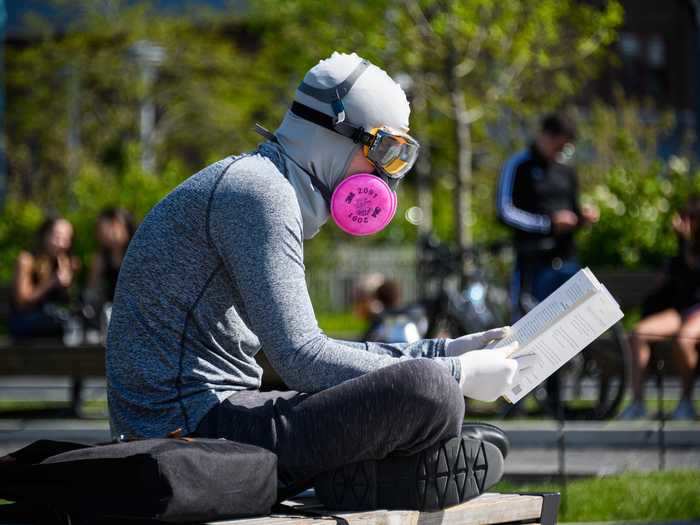 A person wears a protective face mask and goggles while reading a book in Domino Park.