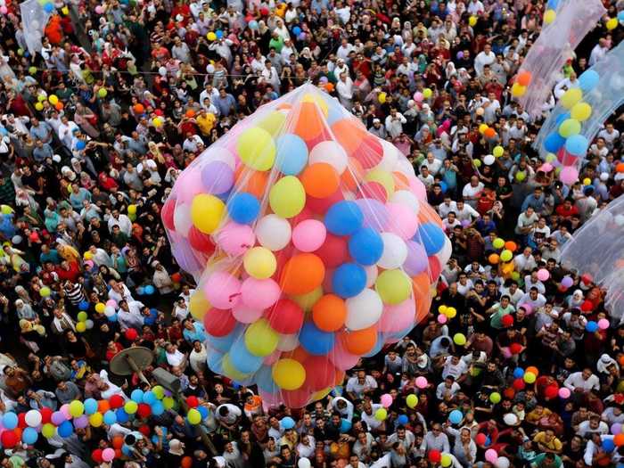 Crowds gather at a public park outside of a mosque in Cairo, Egypt to catch balloons that are released after Eid al-Fitr prayers.