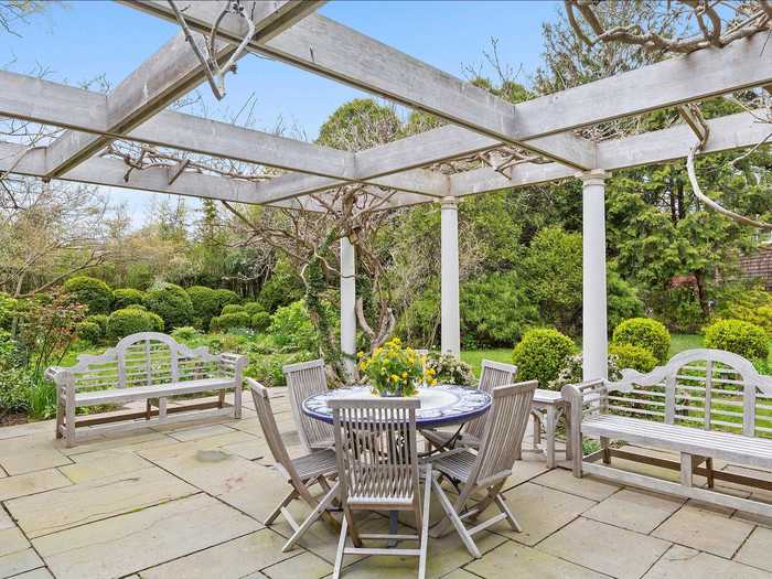 The sun room opens up to a pergola-covered terrace surrounded by greenery.