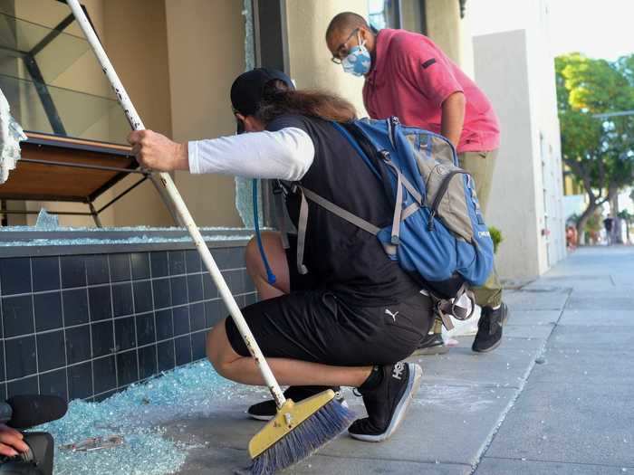 The store owner looked on in shock, noting the looters took his monitors but left his computer inside. By 7 a.m., he had yet to go inside the store. Outside, three neighborhood volunteers gathered to assist in the cleanup effort.