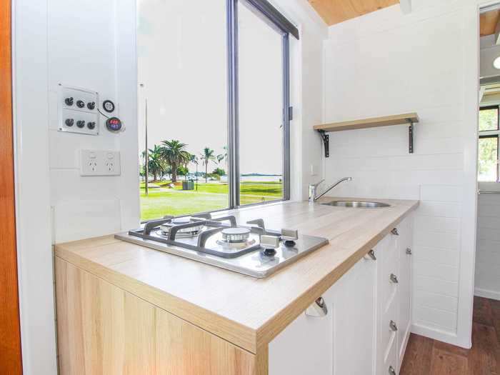 The kitchen — which is next to the living room and entry door — is equipped with a gas cooktop, countertop, sink, several storage drawers, and a shelf.