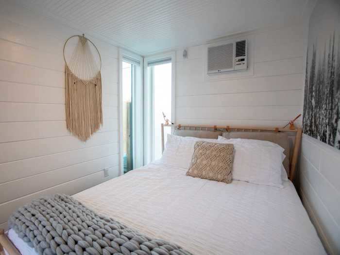 The simple bedroom has a queen sized bed and a small wardrobe with shelves and hangers.