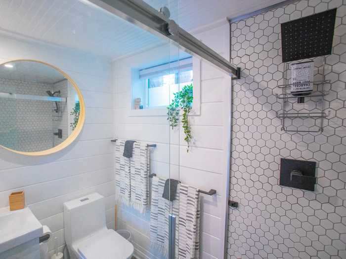 The shower has hexagonal black and white tiling that compliment the rest of the black, white, and wood-themed bathroom.