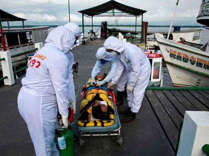 In this photo, healthcare workers carry a 79-year-old infected person onto a stretcher before transferring him to the nearest hospital via boat.