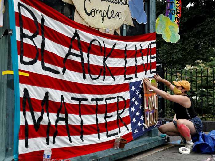 Signs that read "Black Lives Matter," "Defund the Police," and "We keep us safe," adorn the exterior of the occupied area.