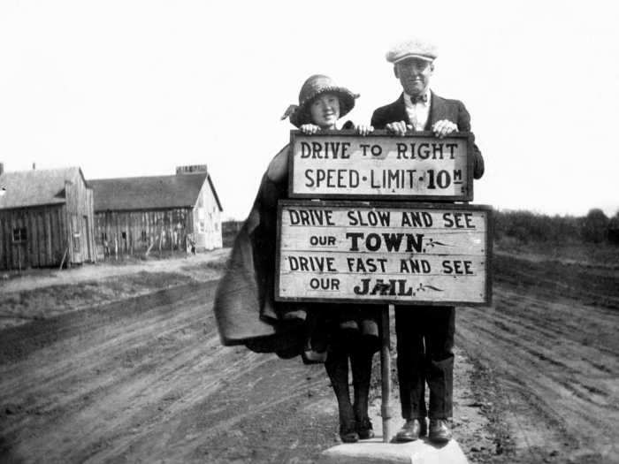 Pictured in Cordell, Oklahoma, in 1920, two people pose by a sign that discourages speeding.