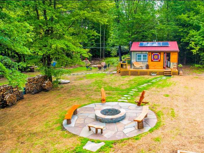 Tucked away in a Catskills clearing, this tiny house with orange walls and a red roof stands out from the surrounding greenery. It comes with a stone fire pit out front, plus a private garden and multiple greenhouses.