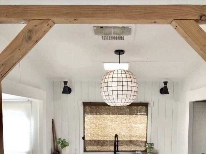 The farmhouse-style kitchen now has a large, modern sink and wooden beams in the entryway.