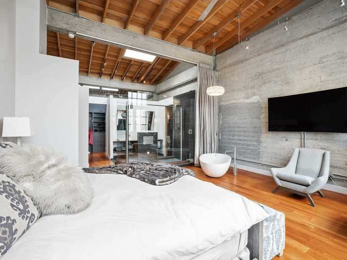 Concrete walls and the ceiling beams contrast with comfortable bedroom furniture.