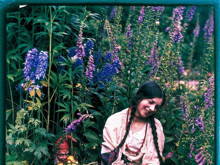 This portrait by British amateur photographer Emma Barton, also known as Mrs. G. A. Barton, shows a woman sitting in a garden surrounded by colorful flowers.