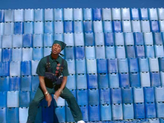 Pharrell performs in front of a wall of water jugs.