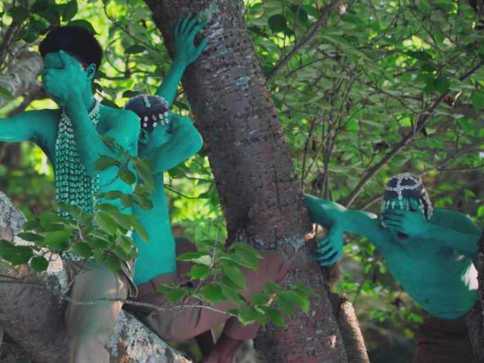 In the next scene, people covered in blue-green paint are adorned with cowry shells.