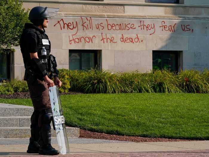 Officers stand in front of the courthouse in riot gear on Monday. Spray painted messaging from protesters on the building reads: "They kill us because they fear us, Honor the dead."