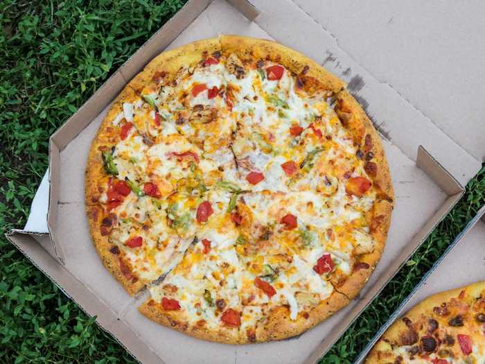 The chicken taco pizza is made with taco seasoning, grilled chicken, onions, green peppers, tomatoes, provolone, cheddar, and American cheese.