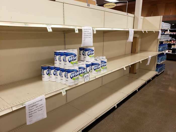 Signs reading "Limit One Package of Bathroom Tissue — We want to be able to serve everyone" hang from empty shelves in a Saline, Michigan grocery store on March 22.