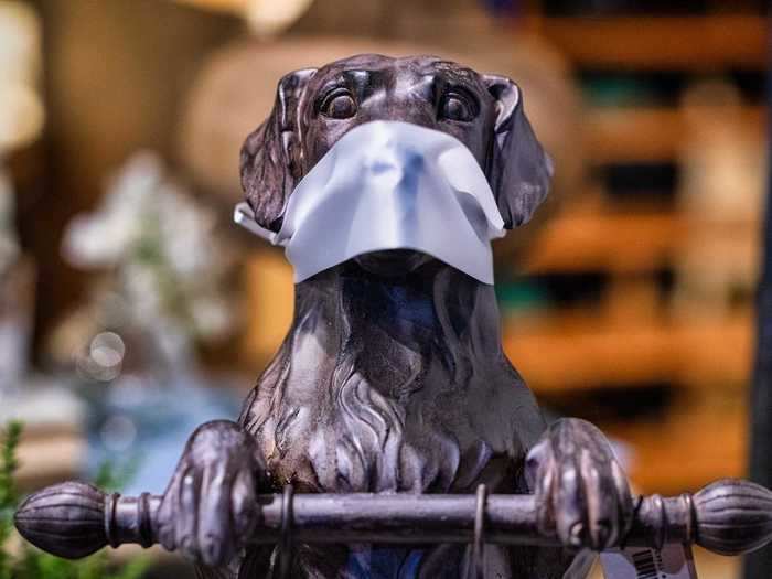 A wooden statue of a dog in the window display of a boutique shop in Bardstown, Kentucky displays a mask to remind reminds customers to put on their masks before entering.