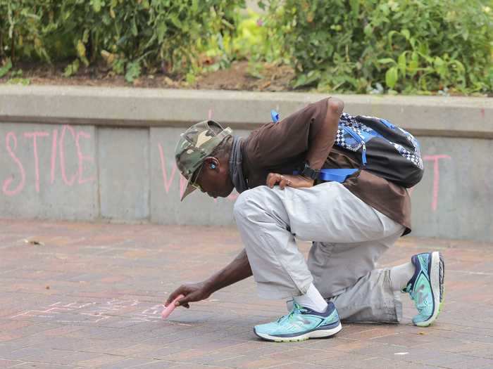 Mauro Jones, 61, of Louisville writes, "The laws were meant to slaughter us," with chalk on the ground in Jefferson Square Park.