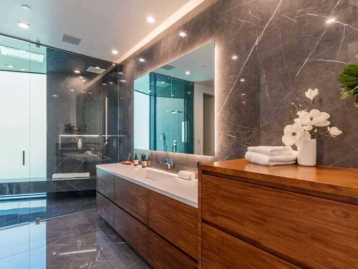 The modern bathrooms feature large mirrors and commercial-grade steam showers. The house also has three powder rooms with stone sinks and LED mirrors.