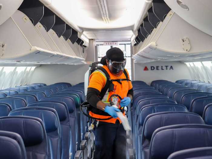 A cleaner walks through the cabin spraying all surfaces, including inside the overhead bins,