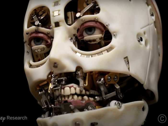 The robot has all the components of a human face, such as eyelids, eyes, a nose, and a mouth with teeth and gums.