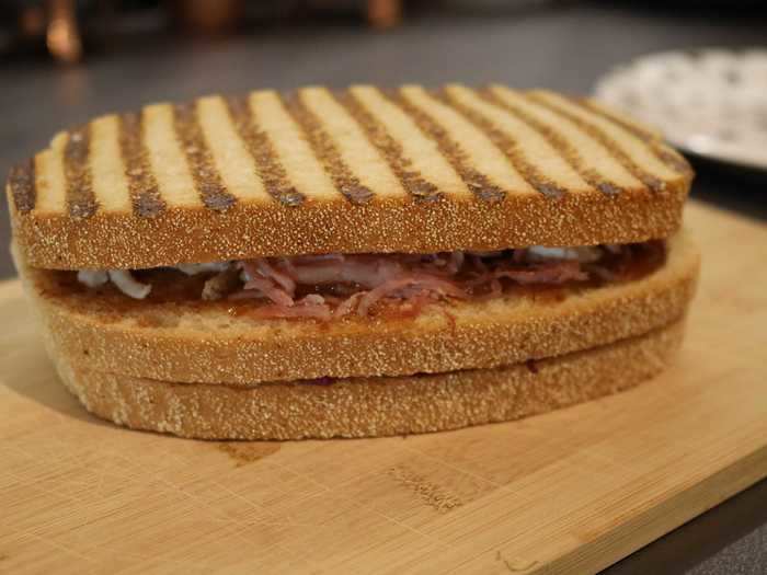 The sandwich has a top layer of pulled ham hock and turkey, a bottom layer of smoky butternut squash, red cabbage, and cheddar cheese, and the all-important slice of sourdough soaked in turkey and cranberry gravy in the middle.