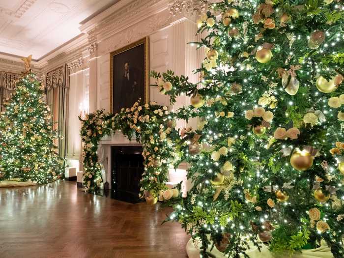 The State Dining Room is decked out in garland and multiple trees with gold ornaments.