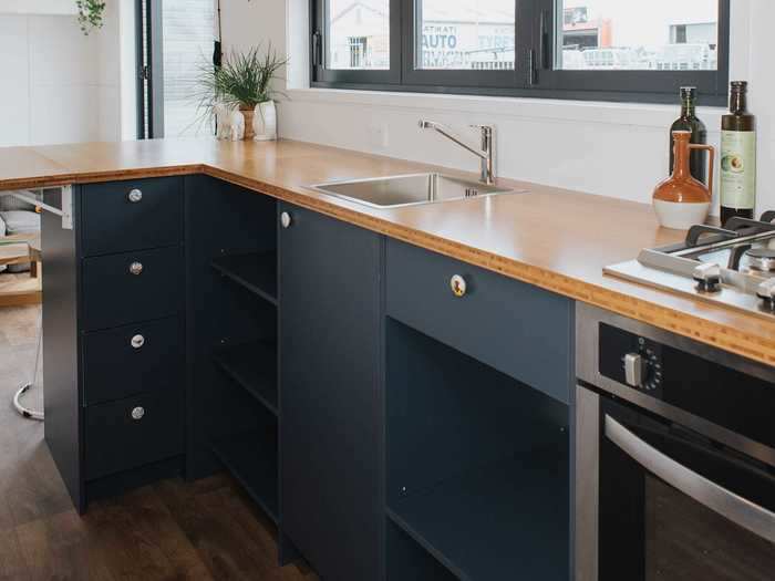 The cooking area includes a refrigerator, a oven, a four-burner gas stovetop with a range hood, and a sink.