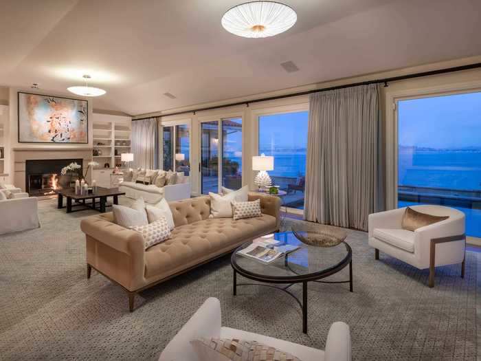 The living room, located at the heart of the home, has a stone fireplace, custom built-in storage space, and glass doors and windows that offer panoramic views of the Bay.