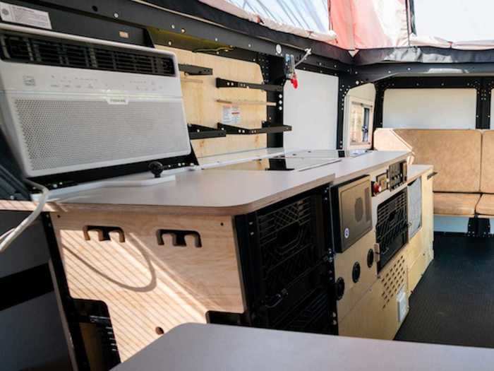 The kitchen specifically has a sink, a two-burner stovetop, a more durable backsplash, a cooler with a 12-volt outlet, shelves, and a "storage tower" made of milk crates and bungee cords.