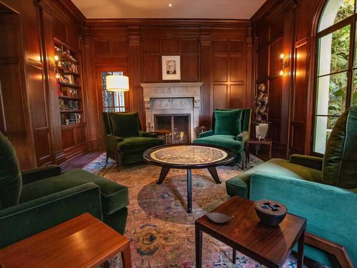 The den features warm wood walls, green velvet chairs, and a fireplace.