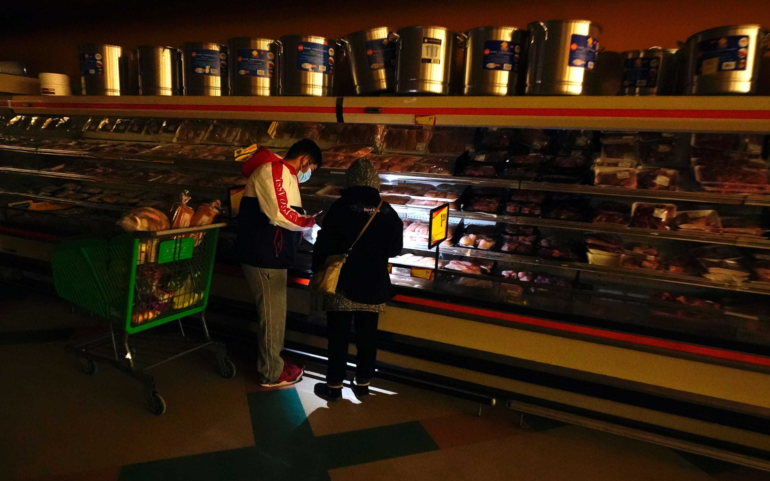 Customers use the light from a cell phone to look in the meat section of a grocery store Tuesday, Feb. 16, 2021, in Dallas. Even though the store lost power, it was open for cash only sales.