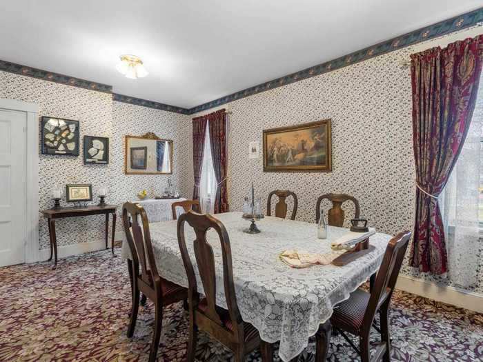 The formal dining room, wrapped in floral wallpaper and stately red drapes, can seat at least six people.