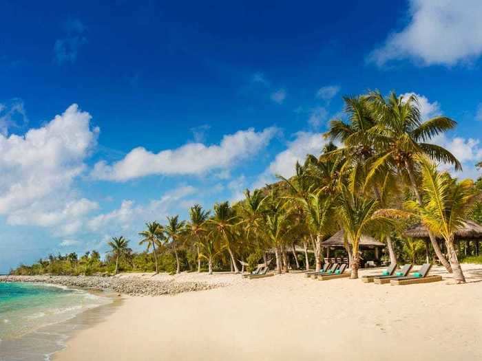 The pristine private beach is lined with palm trees and beach loungers.