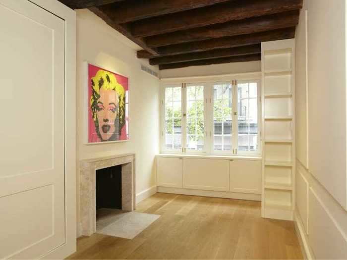 Upstairs, the master bedroom has a bookshelf, a fireplace, and windows looking out onto Bedford Street.