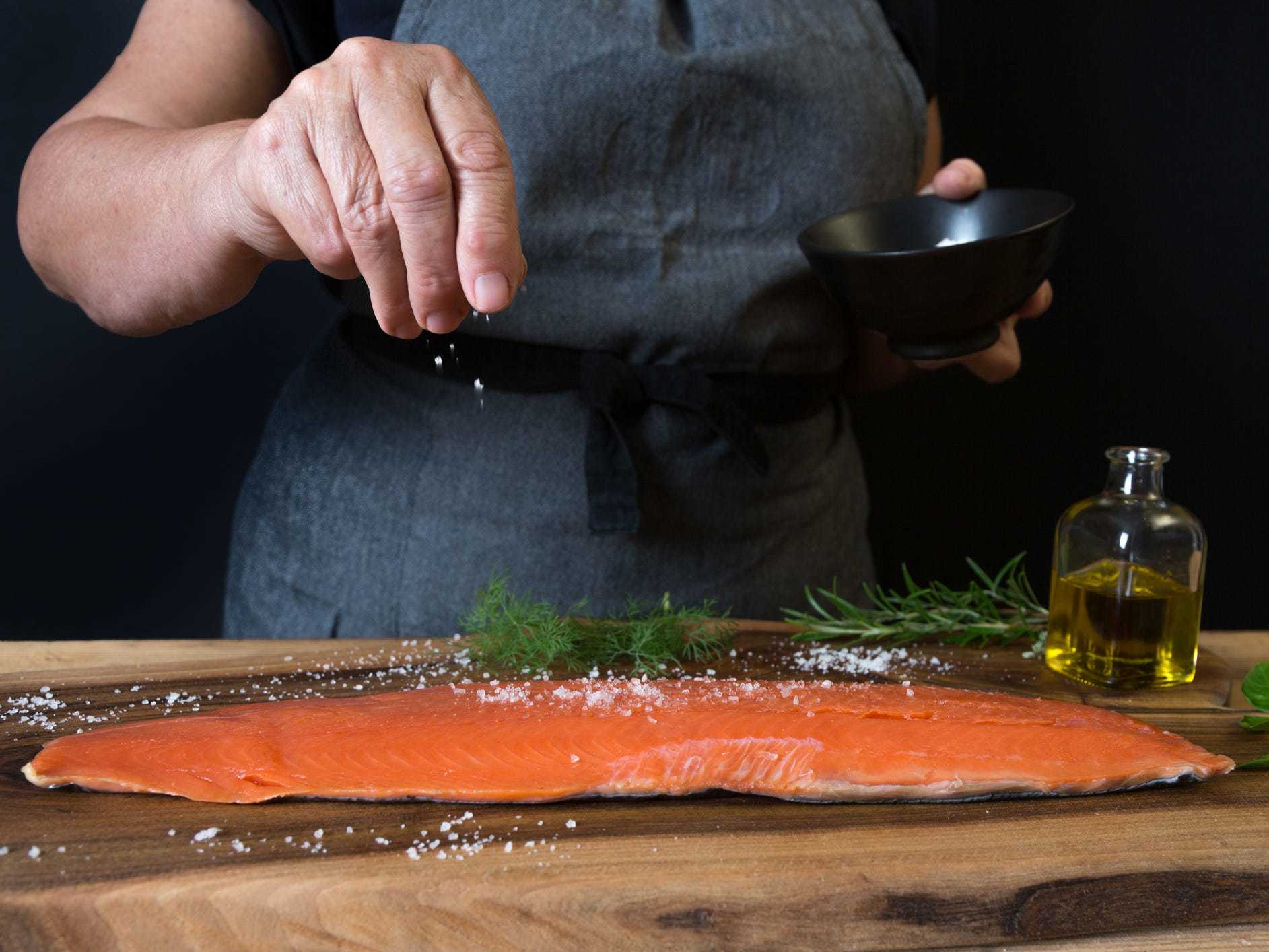 A home cook salting a salmon filet from above