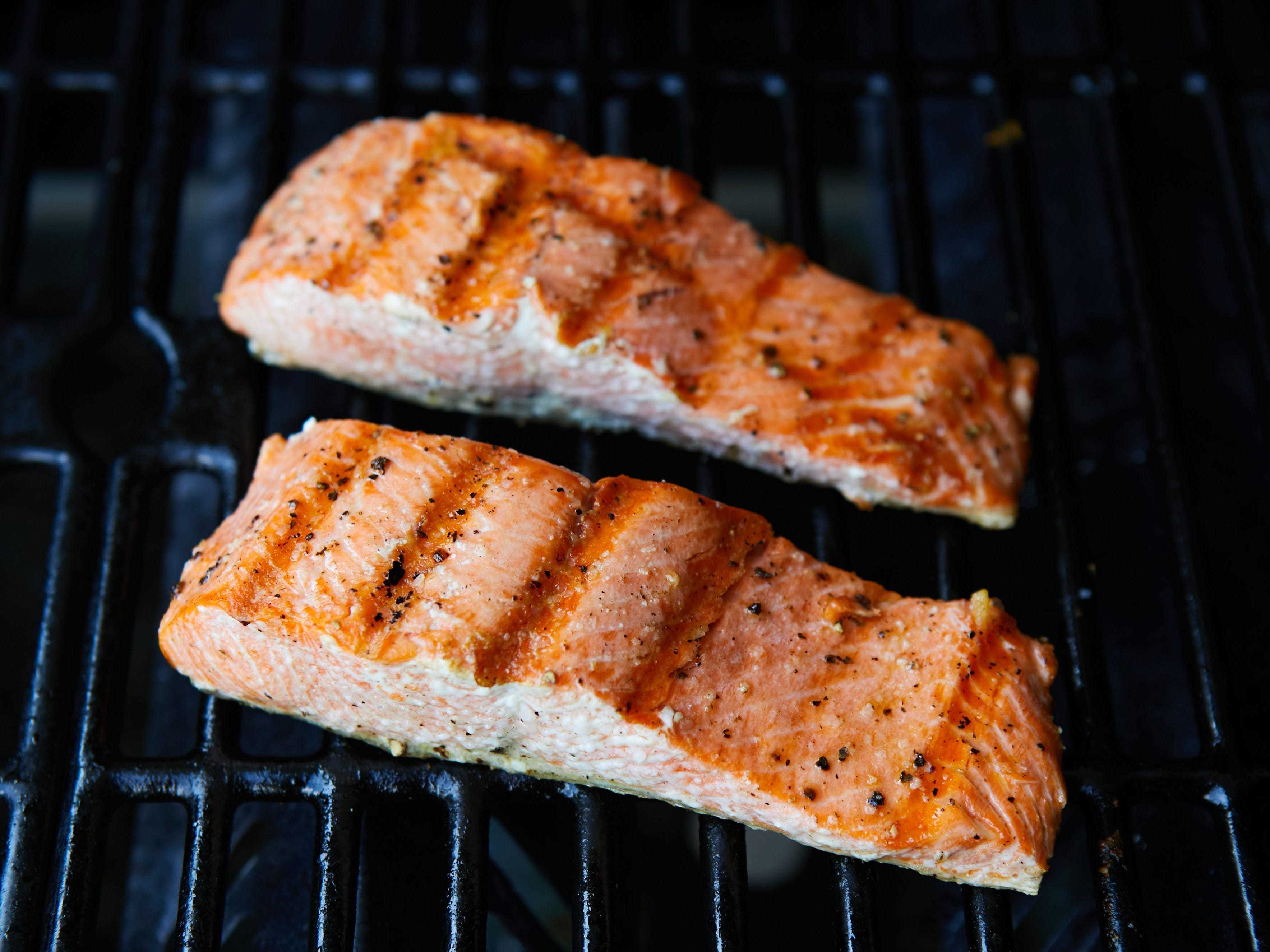 Two grilled salmon filets with char marks sitting on top of a grill grate