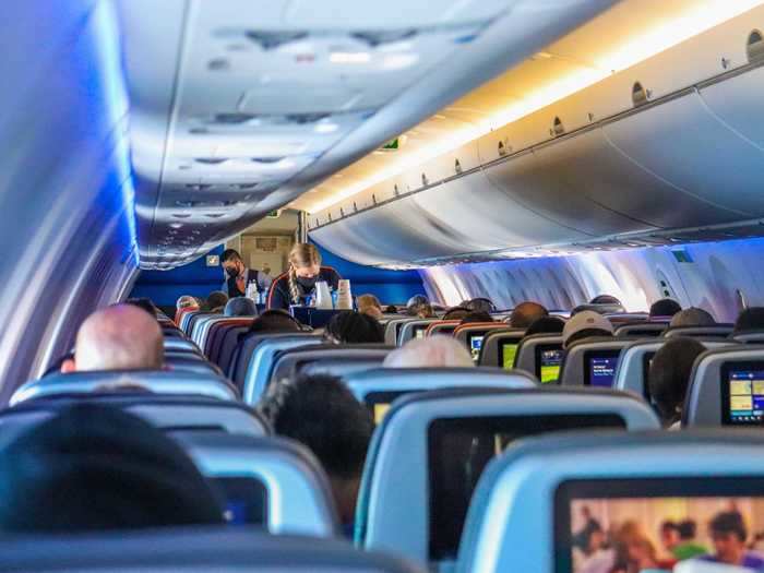 Flight attendants serve drinks from a trolley on this aircraft. One starts from the front while another from the back to minimize wait times.