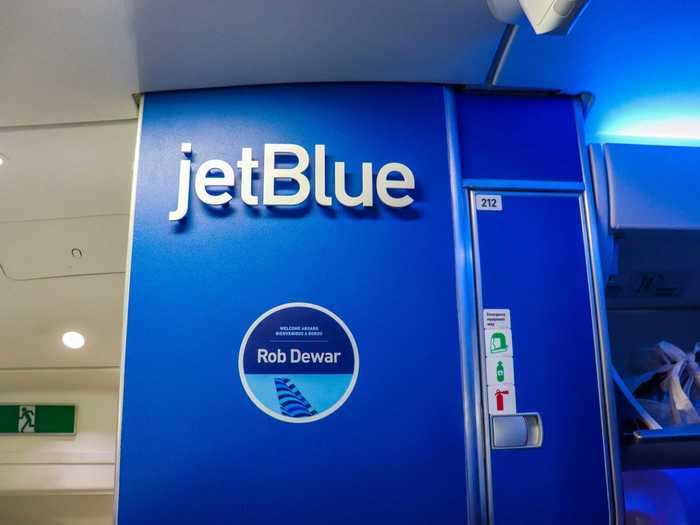 A brilliant blue galley wall greets customers with JetBlue branding and the name of the aircraft. JetBlue named its first A220 after Rob Dewar, the vice president and general manager of the CSeries program for Bombardier. Much like the aircraft, Dewar now works for Airbus.