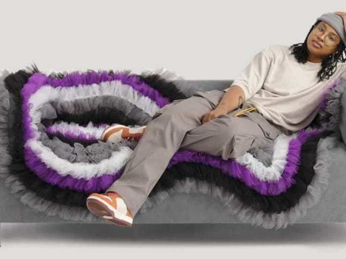 The loveseat that takes after the asexual flag is decorated with purple, black, gray, and white ruffles.