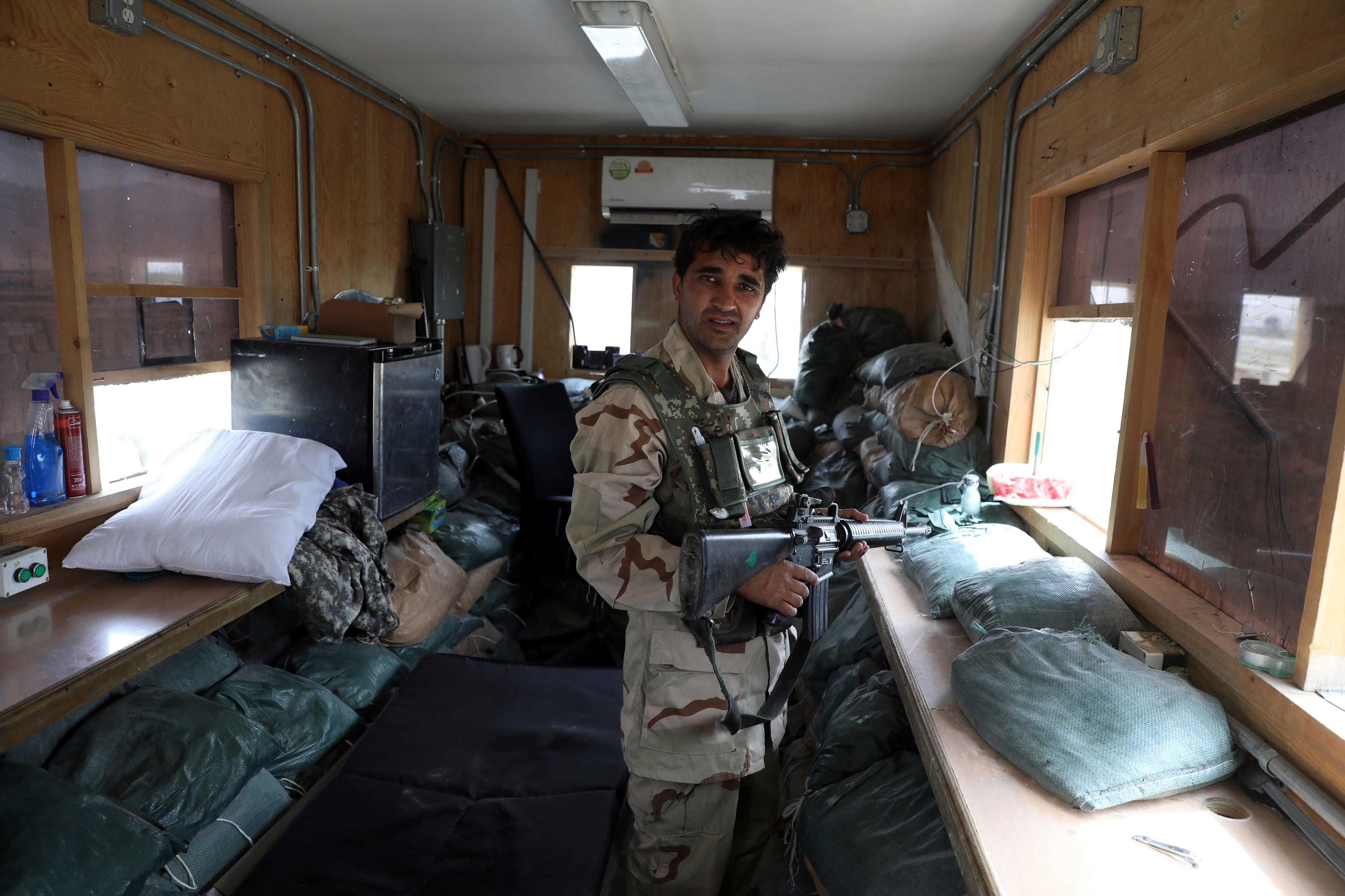 An Afghan security forces member holding a firearm and standing among items like pillows and bags left behind by US troops.