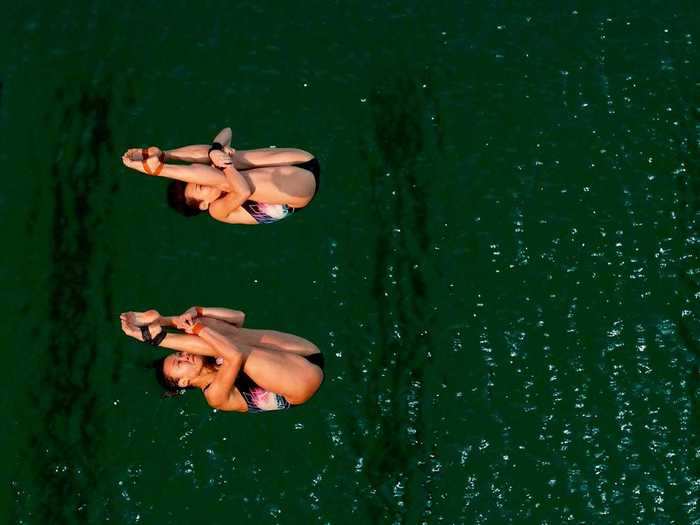 Divers plunge into the mysteriously green pool water.